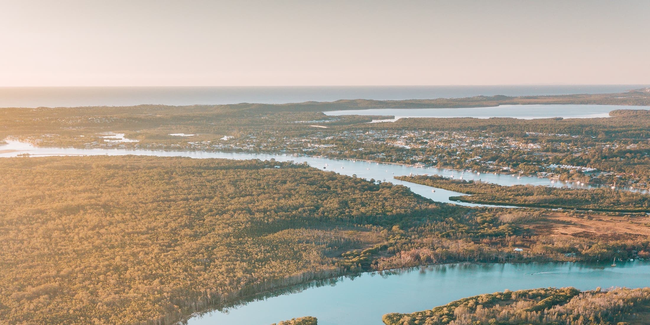 The Noosa River seen from the air in early light, winding past bushland towards Noosaville and the coast